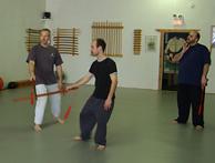 In the Kwoon, Introduction to Tai Chi Straight Sword (March 2007): Demonstrating Pushing Sword with Si-Hing Joel Valerio and Water Tiger student Ed Merchant watching, McElroy Laoshi (L) shares the various Post-It notes of the exercise  step through the mat, move with the whole, flow, relax, breathe, maintain edge-to-edge contact, eyes up, etc.