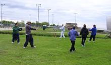 Tai Chi in the Park (May 19, 2007): Using a broadsword as a centering point for a circle, Laoshi Laurince McElroy (in light grey) helps the group to feel a little feline while playing the Tiger Walks from the Five Animal Frolics on a cloudy May morning in the park.