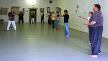 In the Kwoon, Tai Chi Qigong Warming Up (May 2007): A spectrum of Water Tiger students  most from the various studio classes and one from the program at Sachem Public Library  follow McElroy Laoshi (L) as he leads Coiling Forward and Backward from the simple yet complex Tai Chi Qigong Warming Up set during the May installment of the monthly seminar series.