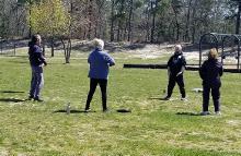 A male faciltator offers instruction to a small group of event participants in a stationary Qigong set.