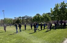 A female workshop facilitator leading a group of event partiipants through an empty-hand T'ai Chi Ch'uan form.